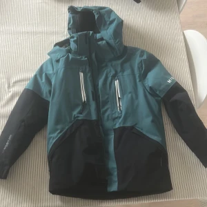 Skidjacka med tillhörande byxor - Snygg skidjacka från McKinley i gröngrått. Tejpade dragkedjor. Jackan har lång ärm, flera fickor och sportig design. Perfekt för dig som vill vara både varm och sportig i skidbacken! Svarta skidbyxor som hör till i samma storlek. Mycket bra skick, 300kr för både jacka och byxor!
