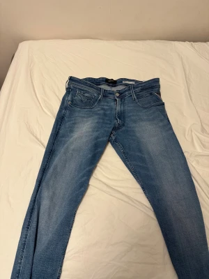 Replay Anbass ljusblå slim jeans - Säljer ett par Replay Anbass jeans i ljusblå tvätt. Modellen är slim fit med klassiska fem fickor, dragkedjegylf och snygga detaljer på bakfickorna. Perfekta för dig som gillar en smalare passform och stilren look. Byxorna är ungefär 32 i längd för de klippte byxorna i de butiken jag köpte dom ifrån för de va lite för långa för mig då