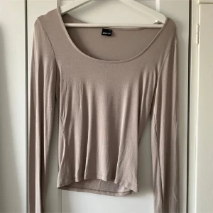 Beige långärmad topp Gina Tricot - Superfin beige långärmad topp från Gina Tricot med rundad, vid urringning och slitsdetalj vid ärmsluten. Tunn och mjuk i materialet, perfekt att styla med jeans eller kjol. Enkel och stilren design som funkar året runt.