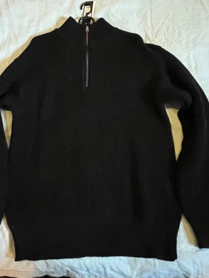 Svart stickad tröja med half zip - Svart stickad tröja från 157 med ribbad struktur och half zip framtill. Tröjan har hög krage och långa ärmar, perfekt för kyliga dagar. Enkel och stilren design som funkar till många olika outfits.