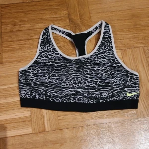Nike sport-bh med djurmönster - Nike Dri-FIT sport-bh i svart och vitt med coolt djurmönster och neongul logga. Brottarrygg och elastisk kant för extra stöd. Perfekt för träning och aktiva dagar.