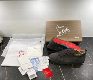 Grå mocka sneakers från Louboutin - Snygga grå sneakers från Christian Louboutin i mjuk mocka med klassisk röd sula. Modellen har rund tå, platt sula och snörning. Insidan är beige och detaljerna är diskreta men lyxiga. Perfekt för dig som gillar exklusiva märken och stilren design.
