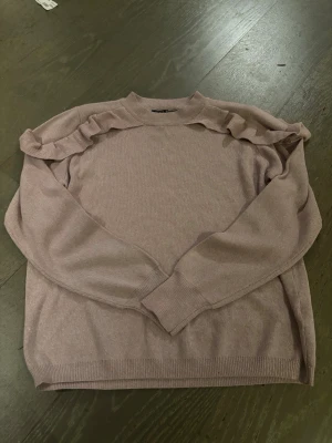 Ljusrosa stickad tröja med volang - Supersöt ljusrosa stickad tröja från Soul River med volangdetaljer längs axlarna. Tröjan har rund hals och långa ärmar med ribbade muddar. Perfekt för dig som gillar en enkel men ändå lite extra look. Strl xl på den men verkligen liten