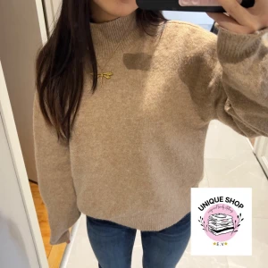 Beige stickad polotröja - Mysig beige stickad polotröja med ribbad hals och muddar. Tröjan har en loose passform och långa ärmar, perfekt för kyliga dagar. Materialet känns mjukt och värmande, och färgen är neutral vilket gör den enkel att matcha med jeans eller andra plagg.