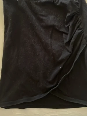 Svart omlottkjol i bomull XS - Svart kortkjol från Cubus, storlek XS. Kjolen har omlottdesign med lätt rynkade detaljer på sidan för en snygg och trendig look.