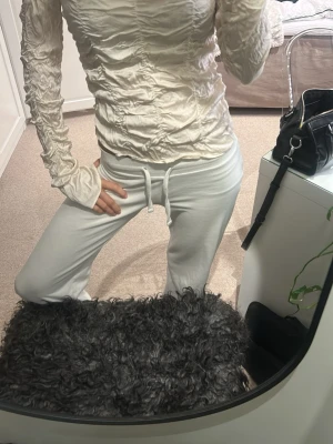 Vit omlott långärmad topp - Säljer en vit långärmad topp med omlott-effekt och snygga rynkade detaljer över hela plagget. Toppen har en slim passform och är tillverkad i ett glansigt syntetmaterial som ger en cool och modern look. Perfekt att styla med jeans eller kjol för en trendig outfit.