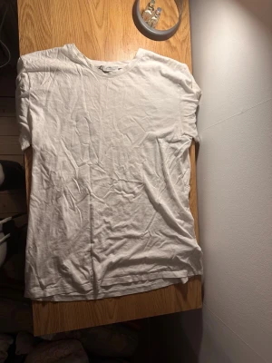 Vit t-shirt  - Säljer en vit t-shirt med ett unikt konstnärligt tryck i silver på ryggen. Klassisk rund hals och korta ärmar. Tillverkad i mjuk bomull som känns skön mot huden. Perfekt för dig som gillar stilrena plagg med en twist.