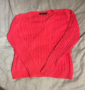 Rosa stickad tröja från Polo Ralph Lauren - Säljer en snygg rosa stickad tröja från Polo Ralph Lauren med klassiskt kabelmönster. Tröjan har v-ringad hals och långa ärmar, perfekt för att hålla dig varm under kyliga dagar. Ribbstickade muddar vid ärmslut och nederkant ger en schysst passform.
