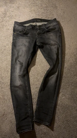 TOS jeans  - Svarta slim-fit jeans från Tiger of Sweden med snygg tvättad look och klassiska fem fickor. Jeansen har smal passform och är tillverkade i jeansmaterial med diskreta slitningar. Perfekt för dig som gillar stilrena och moderna jeans.