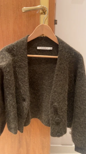 Mörkgrön stickad kofta från Gestuz - Säljer en mysig mörkgrön stickad kofta från Gestuz. Koftan har en loose passform, lång ärm och knappar framtill. Materialet är fluffigt och ger en skön känsla, perfekt för kyliga dagar. Enkel att matcha med jeans eller kjol.