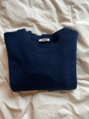 marinblå stickad tröja i 100% merinoull  - En marinblå stickad tröja i 100% merinoull från DAGMAR. Tröjan har krympt i tvätten och passar som en S, se sista bilden för passform. Har även sytt igen ett hål i armhålan som inte syns. Tröjan är annars i ett bra skick!   Skriv vid frågor😊