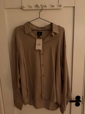Beige skjorta från H&M i viskos - Säljer en beige skjorta från H&M i storlek L, tillverkad av 83% ECOVERO viskos. Skjortan har klassisk krage, knappar framtill och lång ärm. Regular fit med lätt struktur i tyget som ger en chill och modern vibe.