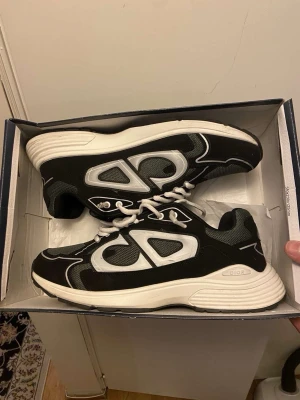 Svarta Dior sneakers med vit sula - Säljer ett par snygga Dior sneakers i svart och vitt med chunky vit sula. Skorna har meshpaneler och detaljer i syntet samt tydlig Dior-logga på sidan. Klassisk snörning och rund tå. Perfekta för dig som gillar statement sneakers.