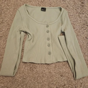 Gullig ljusgrön ribbad croppad topp Gina Tricot - Superfin ljusgrön croppad topp från Gina Tricot med ribbad struktur och rundad halsringning. Toppen har långa ärmar och fem knappar framtill som ger en chill vibe. Endast använda ett fåtal gånger och i mycket bra skick. Nypris runt 150 kr.
