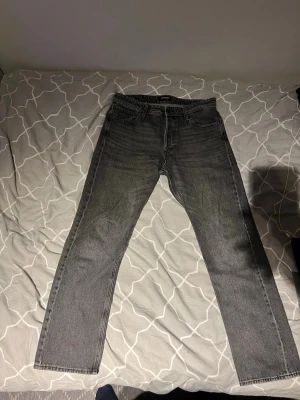 Jack & Jones mörkgrå jeans  - Säljer ett par Jack and jones jeans i mörkgrå tvätt med klassisk femficksdesign och raka ben. Jeansen har normal passform och är tillverkade i slitstarkt bomullsmaterial. Perfekt för dig som gillar tidlös stil och vill ha ett par jeans som funkar till allt.
