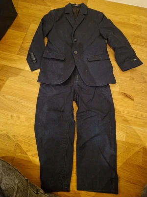 Mörkblå kostym från Hugo Boss slim fit - Säljer en stilren mörkblå kostym från Hugo Boss i slim fit-modell. Kavajen har klassisk krage, två knappar framtill, tre knappar vid ärmslut och fickor med lock. Materialet är mjukt och känns lyxigt. Perfekt för dig som vill ha en snygg och modern look.