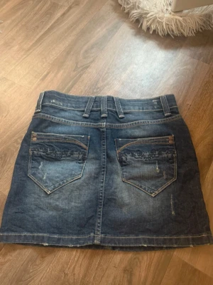 Mörkblå jeanskjol från Lindex Str S - Säljer en mörkblå jeanskjol från Lindex i klassisk denim med slitna detaljer och broderade bakfickor. Super snygg💕