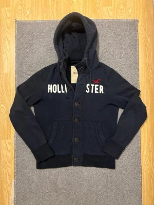 Vintage Hollister Cardigan Med Knappar (sällsynt)  - Väldigt sällsynt och vintage Hollister hoodie med knappar | Tröjan är i väldigt bra skick utan defekter! | Längd ≈ 63cm, Bredd armhåla-amrhåla ≈ 53cm | Modell 175cm, 68kg | Hör av vid ytterligare frågor och priset kan diskuteras vid snabbt köp! |