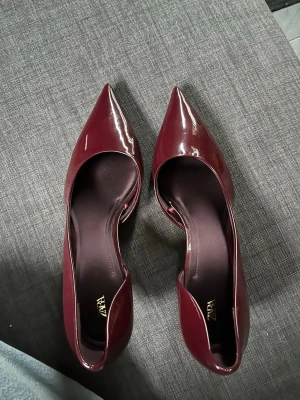 Vinröda lackpumps från Zara - Säljer ett par sprillans nya vinröda pumps från Zara med glansig lackyta och spetsig tå. Skorna har låg klack och en elegant, smal siluett. Materialet är syntet och insidan är också vinröd♥️Så snygga men tyvär lite stora på mig vilket är varför jag säljer. Nypriset runt 500kr💕