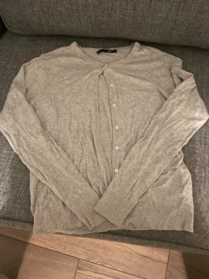 Ljusgrå kofta med knappar - Säljer en enkel och stilren ljusgrå kofta från lager 157. Koftan har långa armar och knappar som gör att man kan ha den knäppt. Funkar för en person med storlek M