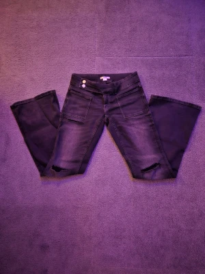 Mörkgråa bootcut jeans från Gina Tricot - Säljer ett par svarta jeans från Gina Tricot i storlek 158. Modellen har bootcut-ben, låg midja och två framfickor. Jeansen har slitna detaljer vid knäna, dubbla silverknappar och dragkedja i gylfen. Materialet är klassisk jeans med stretch. Färgen kanske är lite annorlunda pga ljuset men det går jättebra att fråga om mer bilder om det behövs. Pris går att diskuteras🫰🏻