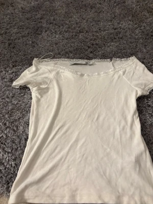 Vit topp med spets från lager 157, storlek S - Säljer en vit topp från lager 157 i storlek S och  är dekorerad med fin spets längs halsringningen och ärmsluten. Modellen är offshoulder och materialet känns mjukt och lätt, perfekt för varmare dagar. Dock finns det en liten * skadad* sak på spetsen 