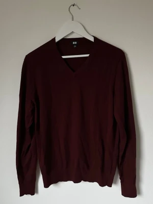 Vinröd v-ringad ulltröja från Uniqlo - Snygg vinröd v-ringad tröja från Uniqlo i 100% ull. Tröjan har lång ärm och klassisk passform, perfekt för lager-på-lager under kyliga dagar. Enkel design utan mönster eller detaljer, vilket gör den lätt att matcha med olika stilar. 5L13