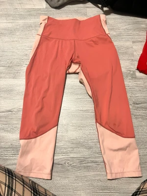 Rosa och korall 3/4 leggings - Snygga leggings i två nyanser av rosa och korall, med hög midja och croppad längd. Perfekta för träning eller chill, tillverkade i mjukt och stretchigt syntetmaterial som sitter skönt mot kroppen.