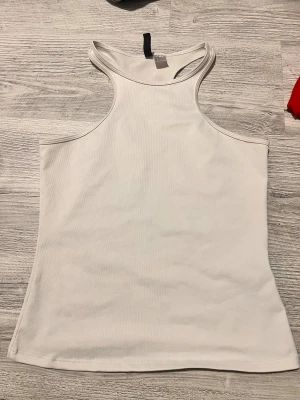 Vit ribbad linnetopp - Säljer en vit ribbad linnetopp från H&M med hög hals och ärmlös design. Toppen har en stilren och enkel look som passar perfekt till jeans eller kjol. Materialet är mjukt och stretchigt för en bekväm passform.