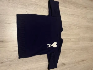 Mörkblå stickad tröja från Ami - Snygg mörkblå stickad tröja från Ami med vit hjärtlogga och bokstaven A på bröstet. Tröjan har långärmade ribbade muddar och ribbad nederkant. Perfekt för dig som gillar stilrena detaljer och vill ha något som sticker ut lite extra.