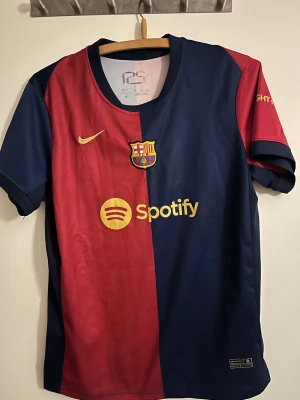 FC Barcelona Nike fotbollströja - Säljer en FC Barcelona matchtröja från Nike med klassisk halva-röd och halva-marinblå design. Tröjan har korta ärmar, rund hals och är gjord i lätt polyester. På bröstet finns klubbmärket, Nike-logga och Spotify sponsor i gult. Perfekt för dig som älskar Barca!