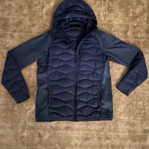 Blå pufferjacka Peak Performance L - Säljer en blå pufferjacka från Peak Performance i storlek L. Jackan har huva, dragkedja framtill och quiltad design på både fram- och baksida. Materialet är syntet och polyester, perfekt för kyliga dagar. Snygg passform och sportig look. Modellen är 189 och den är lite liten så om du är ca 185 så är den perfekt. 