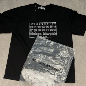 Maison Margiela svart t-shirt - Svart t-shirt från Maison Margiela med ikoniskt tryck av siffror och logga på bröstet. Klassisk rund hals och korta ärmar. Materialet är mjuk bomull och passformen är normal. Perfekt för dig som gillar stilrena designer med en twist.
