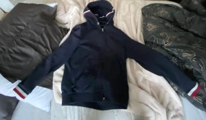 Mörkblå hoodie från Moncler - Snygg mörkblå hoodie från Moncler med dragkedja och huva. Tröjan har långa ärmar med vita och röda ränder vid mudden samt samma randiga detalj på huvan. Moncler-logga på ärmen. Perfekt för dig som gillar stilrena och sportiga plagg.