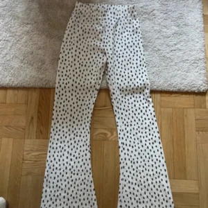 Vita prickiga bootcut byxor - Säljer ett par vita byxor med svarta prickar och bootcut-ben. Byxorna har en medel midja. Perfekt för dig som gillar att sticka ut med mönster och vill ha en cool siluett.