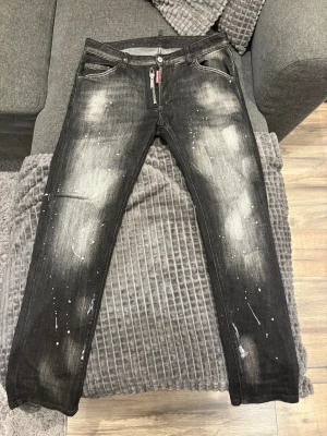 Svarta Dsquared2 jeans med splatter - Säljer ett par svarta jeans från Dsquared2 med coolt blekt och splattermönster. Modellen har klassisk femficksdesign, dragkedja och raka ben. Jeansen är tillverkade i jeansmaterial och har en vit Dsquared2-label bak i midjan. Dem är rätt så små i storleken