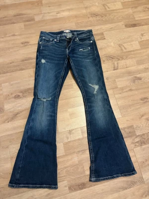 Bootcut jeans från Gina Tricot, M - Snygga blå bootcut jeans från Gina Tricot med slitna detaljer och kontrastsömmar. Lågmidjade och stretchiga.   Använd kanske max 4 gånger.