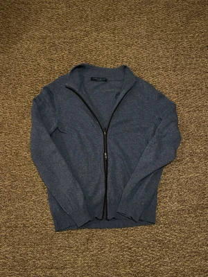 Kofta i kashmir från Libero Milano - Mjuk och stilren grå kofta från Libero Milano i lyxig kashmir. Koftan har hel dragkedja framtill, ribbade muddar och långärmad design. Perfekt för dig som gillar klassisk look med premiumkänsla. Snygg att ha över en t-shirt eller skjorta.