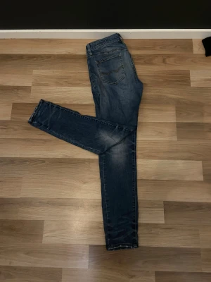 Blå skinny jeans från American Eagle - Säljer ett par blå jeans från American Eagle Outfitters med Extreme Flex. Modellen har smal passform, klassiska fem fickor och snygga slitningar på benen. Perfekt för dig som gillar stretchiga och bekväma jeans med modern look.