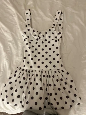Vit prickig kortklänning från Zara - Supersöt vit kortklänning från Zara med svarta prickar och breda axelband. Klänningen har en markerad midja och utställd kjol som ger en lekfull och trendig look. Perfekt för dig som gillar retrovibbar och vill sticka ut lite extra. säljer för mycket då den har slutat säljas, är oanvänt och extremt eftertraktad 💕💕