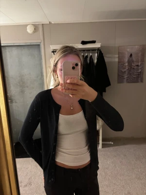 Svart kofta med knappar - En klassisk svart kofta med rund hals och knäppning framtill. Långärmad och i en smidig, tunn stickad kvalitet som passar perfekt till lager-på-lager. Enkel och stilren design som funkar till det mesta.