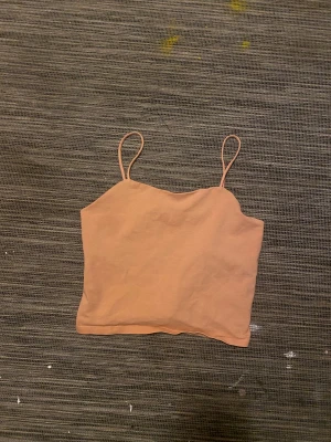 Beige/coral färg linnetopp med smala axelband  - Säljer en enkel och stilren beige linnetopp med smala axelband. Toppen är croppad och har en rak skärning upptill. Tillverkad i mjuk bomull som känns skön mot huden. Perfekt att matcha med jeans eller kjol för en chill look.
