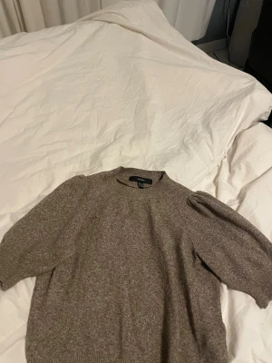 Beige stickad tröja - Mysig beige stickad tröja från Vero Moda i storlek M. Tröjan har rund hals, puffade axlar och ribbade muddar vid ärmslut och nederkant. Perfekt för dig som gillar enkel och stilren design med lite volym på ärmarna.