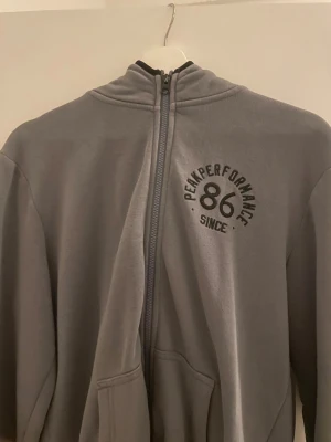 Grå hoodie från Peak Performance - Säljer en grå hoodie från Peak Performance i storlek S. Tröjan har hel dragkedja framtill, fickor och tryck med 'Peak Performance 86' på bröstet. Mjuk insida och klassisk passform, perfekt för chill eller träning.