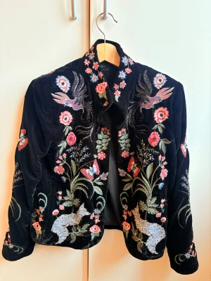 Broderad svart jacka från Zara Woman - Unik svart jacka från Zara Woman med broderade fåglar, blommor och fjärilar i rött, blått och grönt. Jackan är gjord i mjuk (velvet ) sammet och har långärmad passform. Perfekt för dig som vill sticka ut med coola detaljer och färgstarka broderier.