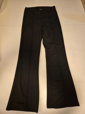 Svarta byxor - Svarta byxor i lite kostym liknande stil med en söm på benens framsida och resår i midjan. Materialet skulle jag beskriva som ett crepe liknande tyg. Använda en gång så skicket är som nytt. Storlek S och ca 105 cm långa totalt. 95% polyester, 5% elastan