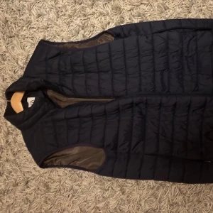 Mörkblå quiltad dunväst från Zara - Snygg mörkblå dunväst från Zara i storlek M. Västen har quiltad design, hög krage och dragkedja framtill. Insidan är brun och materialet känns lätt och smidigt. Perfekt att slänga över en hoodie för extra värme.