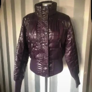 Mörklila pufferjacka från italienska Terranova - Snygg mörklila pufferjacka från Terranova med glansig yta och högt krage. Jackan har ribbade muddar vid ärmslut och midja, samt både dragkedja och knappar framtill. Perfekt för kalla dagar och har en cool, urban vibe.