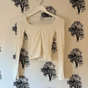 Vit croppad långärmad topp från H&M - Säljer en vit långärmad topp från H&M divided i croppad modell. Toppen har en snygg v-ringad hals och lätt rynkning framtill. Tillverkad i mjuk bomull, perfekt för att styla med jeans eller kjol. Enkel och clean design som funkar till många looks.
