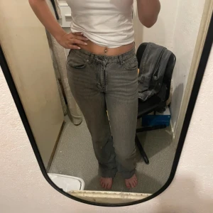 Grå raka jeans med hög midja - Säljer ett par grå jeans med raka ben och hög midja. Jeansen har klassisk femficksdesign, bälteshällor och dragkedja med knapp. Materialet är denim och färgen är en snygg tvättad grå nyans som passar till det mesta.